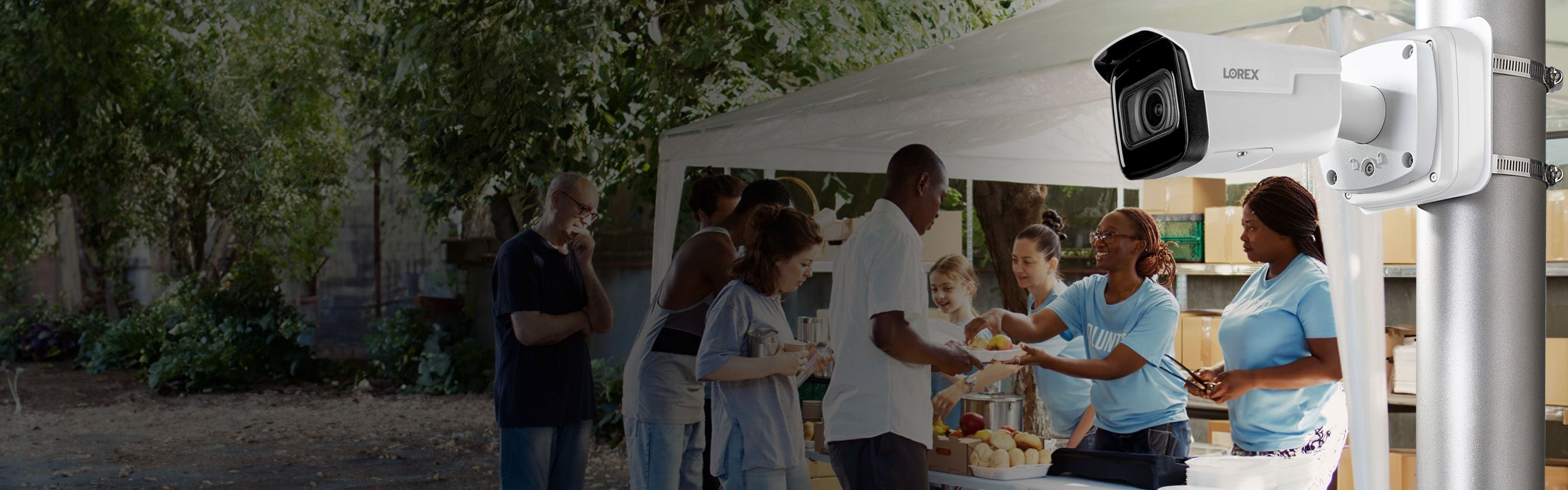 Lorex bullet security camera mounted on a pole, overlooking a group of volunteers serving food at an outdoor community event supporting Lorex for Business Not-For-Profit program